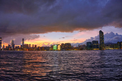 Sea by buildings against sky during sunset