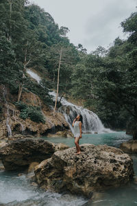 Full length of woman on rock by river in forest