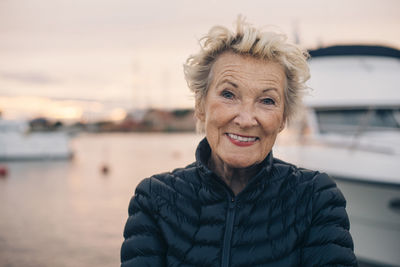 Portrait of senior woman smiling at harbor during sunset