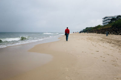 Rear view of men on beach against sky