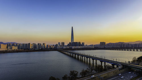 Bridge over river by buildings against sky during sunset