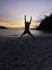 Silhouette man with arms raised on beach against sky during sunset