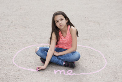 Portrait of girl making chalk drawing while sitting on street