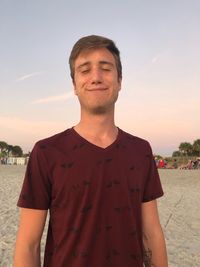 Portrait of young man standing on beach against sky during sunset