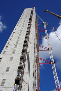 Low angle view of crane by building against blue sky