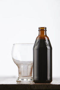 Close-up of drink in bottle by glass on table against white background