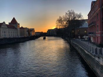 River amidst buildings in city against sky during sunset