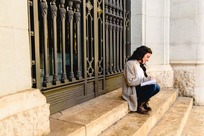 Side view of woman sitting on steps outside building