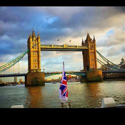 Suspension bridge over thames river against cloudy sky