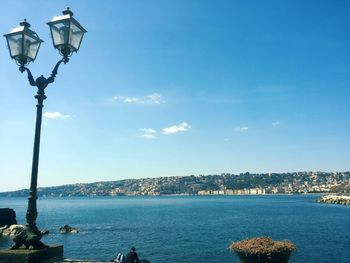 Illuminated street light by sea against blue sky