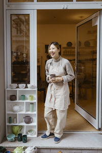Young female potter laughing while standing at workshop doorway