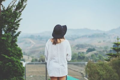 Rear view of woman standing on railing against sky