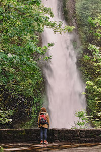 Woman in the raincoat, with a backpack standing near beautiful waterfall in oregon