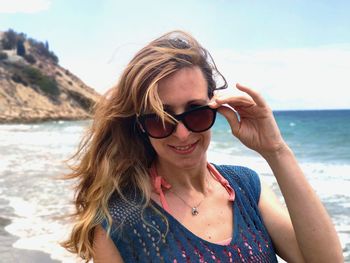 Portrait of young woman wearing sunglasses standing at beach