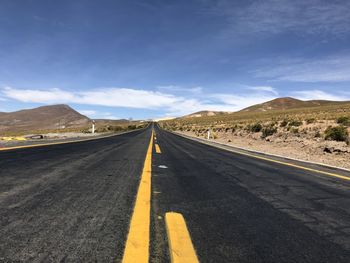 Empty road leading towards mountains against sky