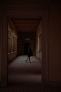 Full length of young woman standing in dark corridor