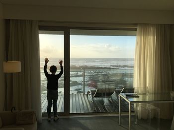 Rear view of boy standing by window against sea