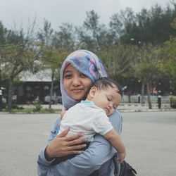 Portrait of smiling mother carrying son while standing on road