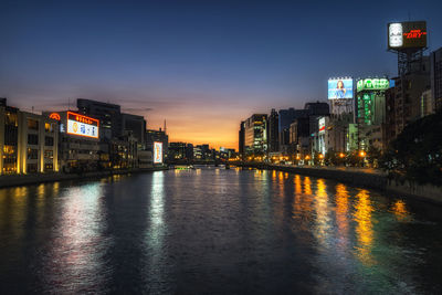 Illuminated buildings by river against sky at night