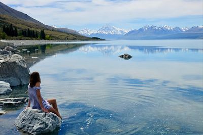 Rear view of woman sitting at lake against mountains