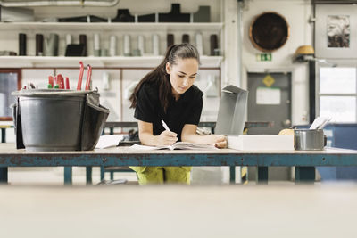 Confident young woman writing in book at workshop