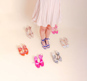 Stylish girl standing in pink pleated dress surrounded by a variety of shoes. 