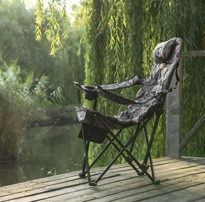 Chair on table by lake against trees