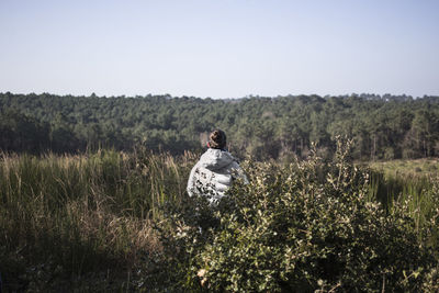 Rear view of woman standing amidst plants against clear sky