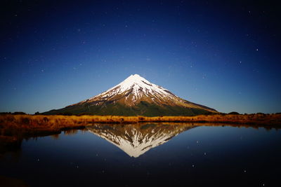 Reflection of mountain in lake against blue sky at night