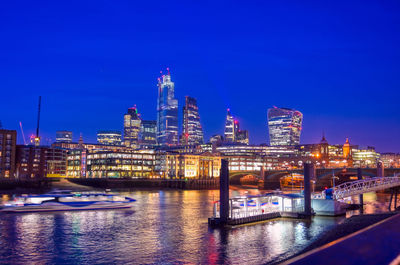 Illuminated buildings by river against sky at night