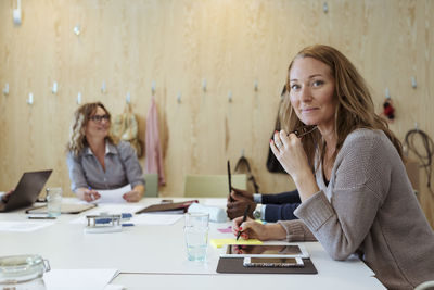 Portrait of confident businesswoman sitting at conference table with colleagues in background