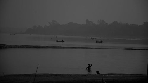 Silhouette people standing on lake against clear sky at dusk