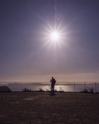 Silhouette man standing on railing against sea against sky