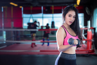 Confident young woman holding dumbbell while exercising in gym