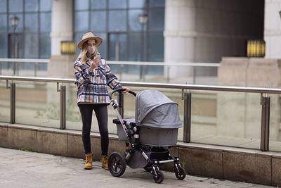 Happy mother walking with stroller in park and using mobile phone. joy of motherhood. stylish woman