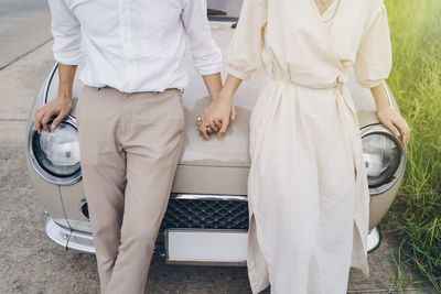 Midsection of couple holding hands while standing by car