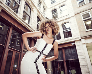 Low angle portrait of beautiful woman standing against building in city