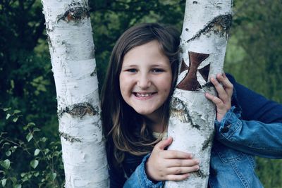 Portrait of smiling girl holding tree trunk