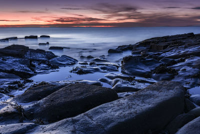 Rocks on beach against sky during sunset