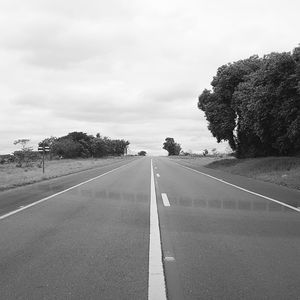 Empty road by trees against sky