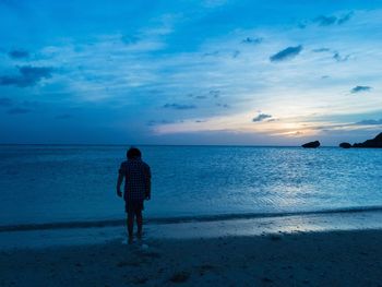 Rear view of man standing on beach against sky