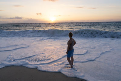 Full length of man standing on beach against sky during sunset