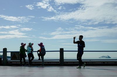 People standing on railing by sea against sky