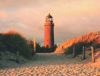 Lighthouse amidst trees and buildings against sky during sunset