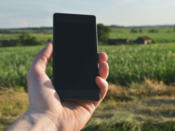 Cropped hand of man holding mobile phone against grassy field