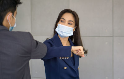 Smiling business person wearing flu mask gesturing against wall