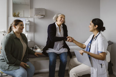 Happy senior woman shaking hand with doctor sitting in clinic