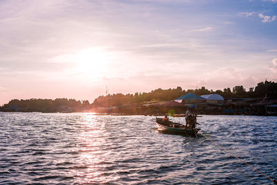 People sailing in boat at sea against sky during sunset