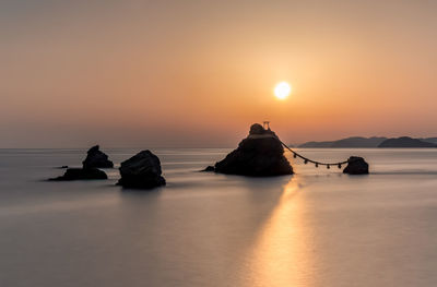 Rocks in sea against sky during sunset