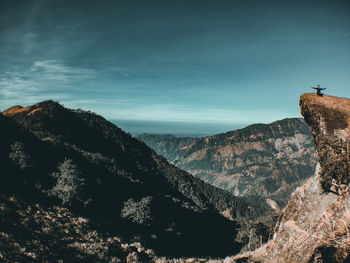 Mid distance view of young man sitting on mountain against sky